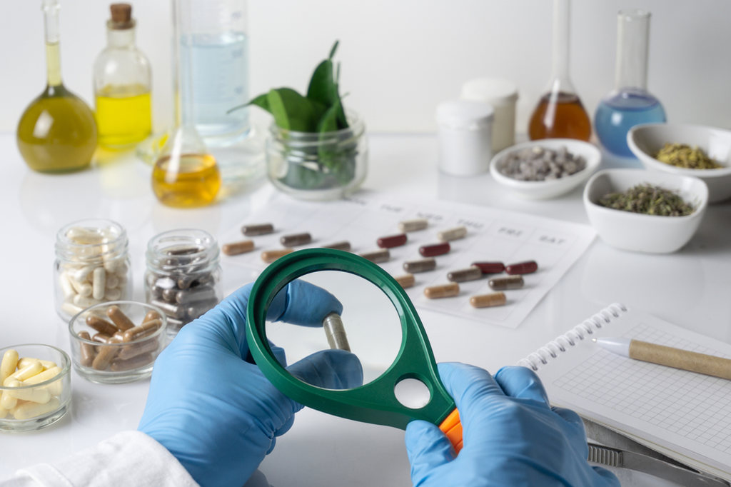 Fabricação de suplemento em cápsula, profissional num laboratório examinando uma cápsula com lupa